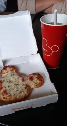 a pizza in a box next to a red coffee cup on a black table top