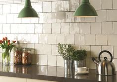 three green lights hanging from the ceiling above a kitchen counter with coffee pots and mugs