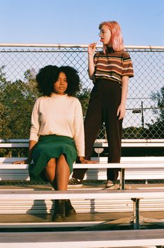 two women are sitting on benches and one is brushing her teeth while the other stands behind them