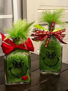 two glass jars with green grass in the shape of grin face and red bow on top