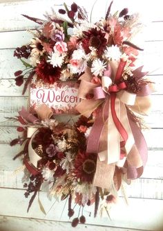 a welcome wreath hanging on the side of a building with flowers and ribbons around it