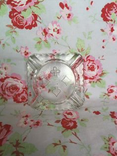 an empty glass ashtray sitting on top of a floral table cloth