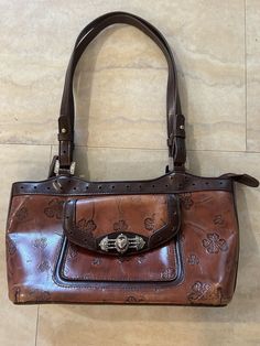 This vintage Marc Chantal handbag features a charming shamrock pattern and silver hardware. The bag is made of high-quality leather and has a zip closure. It measures 13 inches in width, 7 inches in height, and 4 inches in depth, making it a medium-sized bag. The bag's exterior is 2-tone brown and its lining is brown. It has a satchel/top handle bag style and is perfect for women. This bag is a great addition to any collection and is sure to make a statement. Excellent condition few scratches on bottom Green Baguette Bag, Vintage Baguette Bag, Ash Style, Walking Out The Door, Vintage Brown Leather Bag, Shamrock Pattern, Funky Accessories, Handbags Vintage, Make Up Bags