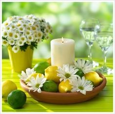 a candle and some lemons in a bowl on a yellow table cloth with daisies