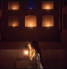 a woman standing in front of a building with lit candles on it's windows