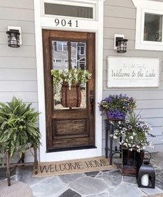 a welcome sign is on the front door of a house with potted plants outside