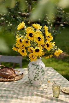 a vase filled with yellow sunflowers sitting on top of a checkered table cloth