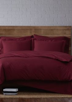 a bed with red sheets and pillows in a room next to a white brick wall