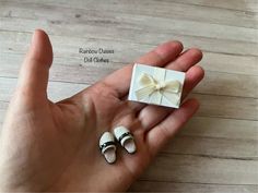 a hand holding a small white box with a bow on it and two tiny shoes