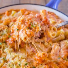 a spoon full of macaroni and cheese being lifted from a bowl with meat sauce