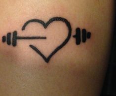 a heart and barbells tattoo on the back of a woman's shoulder