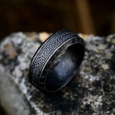 a black ring with an intricate design on it sitting on top of a stone slab