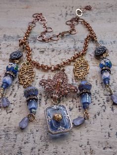 An assemblage of vintage components in a Bohemian style. The central assembled pendant is a vintage to antique fleur dis lis shape copper over brass component to which I've added a vintage German glass intaglio of the Eiffel Tower on the back. It suspends an Art Deco faceted blue glass cabochon in a filigree silver setting. Originally, this pendant would have had a rhinestone in the center, but it was missing, so I've added a gold plated brass filigree bead cap as a focal and to tie it in with the other brass elements in the design. Accompanying pendants are vintage Czech glass buttons, vintage Czech atlas glass and fire polished tulip shaped beads, Japanese 1930s glass beads and vintage lampwork beads with floral detail along with vintage caps and rhinestone rondelles. Length can be adjus Vintage Metal Necklace With Patina, Vintage Patina Metal Necklace, Vintage Silver Copper Necklace, Vintage Copper Necklace In Silver, Vintage Silver Necklace With Copper, Bronze Metal Necklace From Vintage Collection, Artisan Vintage Charm Necklaces, Ornate Antique-finish Copper Jewelry, Vintage Copper Jewelry With Patina