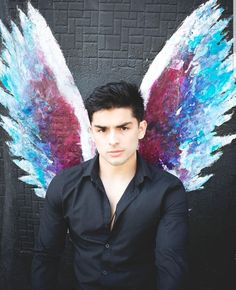 a man standing in front of a wall with an angel wings painted on it's back