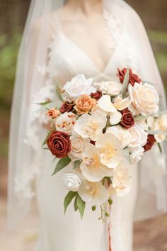 a bridal holding a bouquet of white and red flowers on her wedding day in the woods