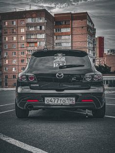 the back end of a black car parked in a parking lot next to tall buildings