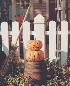 three carved pumpkins sitting on top of a barrel in front of a white picket fence