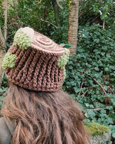 a woman with long hair wearing a crocheted hat in front of some trees