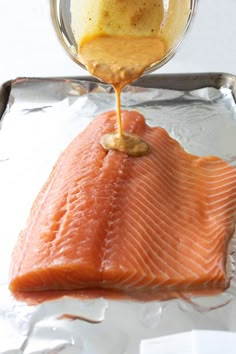 a piece of salmon being drizzled with mustard on top of it in foil