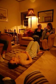 three people are sitting in a living room and one person is laying on the floor