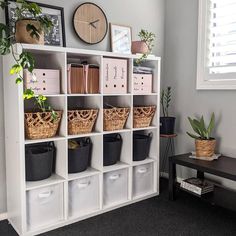 a white bookcase filled with lots of plants and baskets next to a window covered in blinds