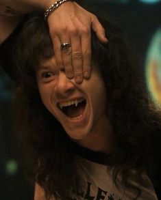 a man with long hair is holding his hands over his head and making a face