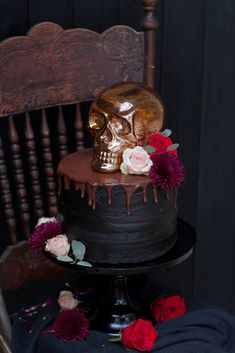 a chocolate cake decorated with flowers and a gold skull topper on a wooden chair