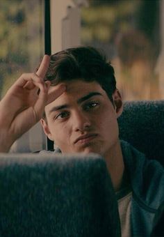 a young man sitting on a bus holding his hand up to his forehead while looking out the window