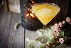 a glass filled with yellow liquid sitting on top of a wooden table next to flowers