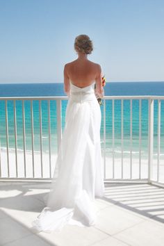 a woman in a white wedding dress looking out at the ocean from a balcony area