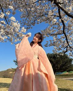 a woman in an orange dress standing under a cherry blossom tree