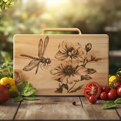 a wooden cutting board with flowers and dragonflies on it, surrounded by fresh vegetables