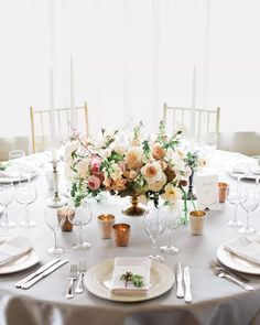 the table is set with white and gold plates, silverware, and floral centerpieces