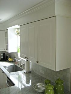 a kitchen with white cabinets and green vases sitting on the counter top in front of the sink