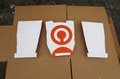 an orange and white sticker sitting on top of a cardboard box next to two pieces of paper