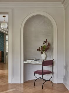 a chair sitting in front of a table with a vase on it