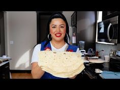 a woman holding up a tortilla in her kitchen