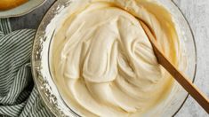 a bowl filled with white frosting next to a wooden spoon on top of a table