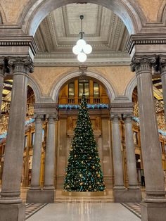 a large christmas tree is in the middle of a room with columns and lights on it