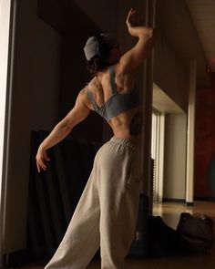 a woman standing in the middle of a room wearing sweatpants and a baseball cap