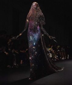 a woman is walking down the runway in a long dress with stars on her body