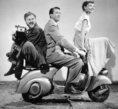 three people riding on the back of a scooter