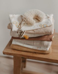 a pile of folded clothes sitting on top of a wooden table next to a stuffed animal