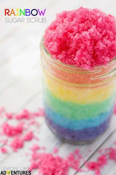 a jar filled with rainbow colored sugar on top of a white wooden table next to pink and blue sprinkles