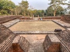 an old brick building with grass in the middle and two people standing on one side