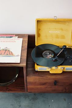 an old record player sitting on top of a wooden table next to a yellow suitcase