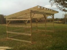 a wooden structure sitting in the middle of a grass covered field next to a tree