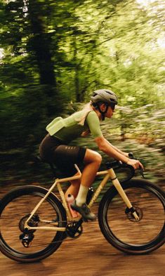 a person riding a bike on a dirt road in the woods with trees behind them