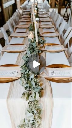 a long table with white chairs and greenery on it