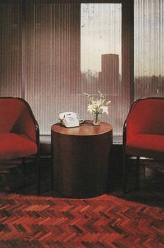 two red chairs sitting next to each other in front of a table with a vase on it